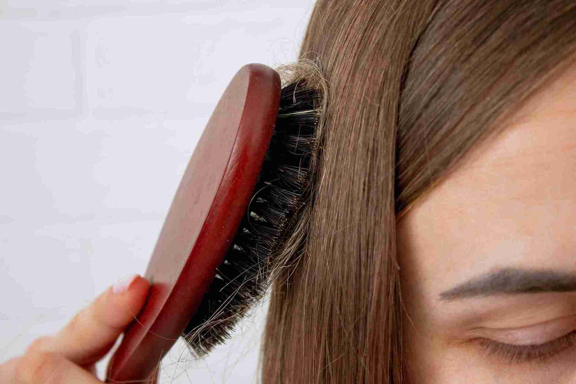Mujer cepillándose el cabello con un cepillo de cerdas negras; se observan mechones atrapados en el cepillo, lo que puede estar relacionado con la alopecia femenina