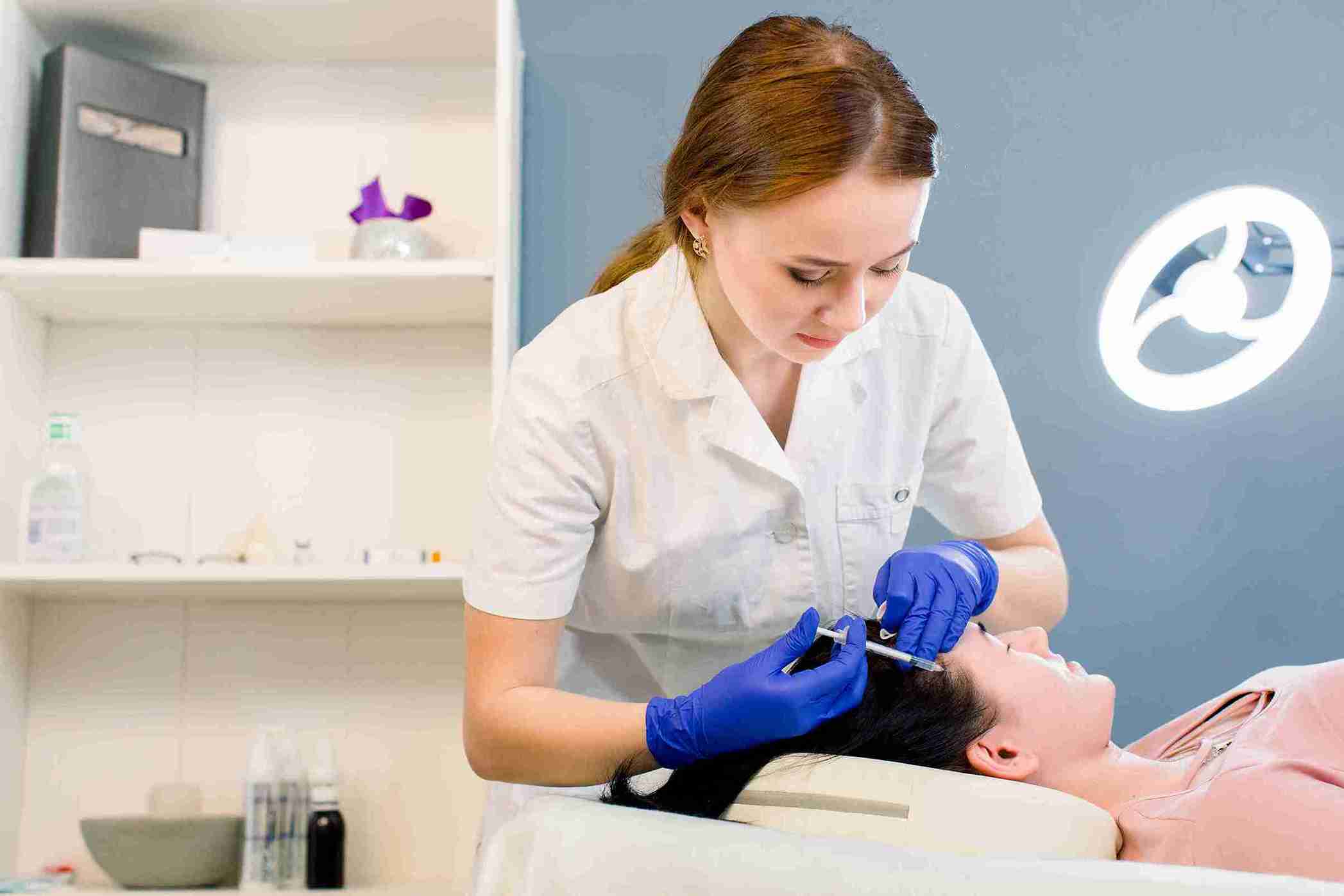 Ärztin führt Mesotherapie bei Haarausfall durch, indem sie einer Patientin mit Handschuhen Injektionen in die Kopfhaut verabreicht.