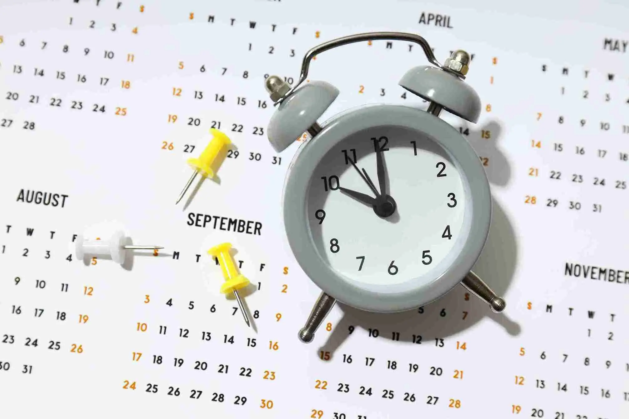 Ein grauer Wecker liegt auf einem Kalender mit markierten Terminen – symbolisch für die Frage Wie lange dauert eine Haartransplantation und den zeitlichen Aufwand des Eingriffs.