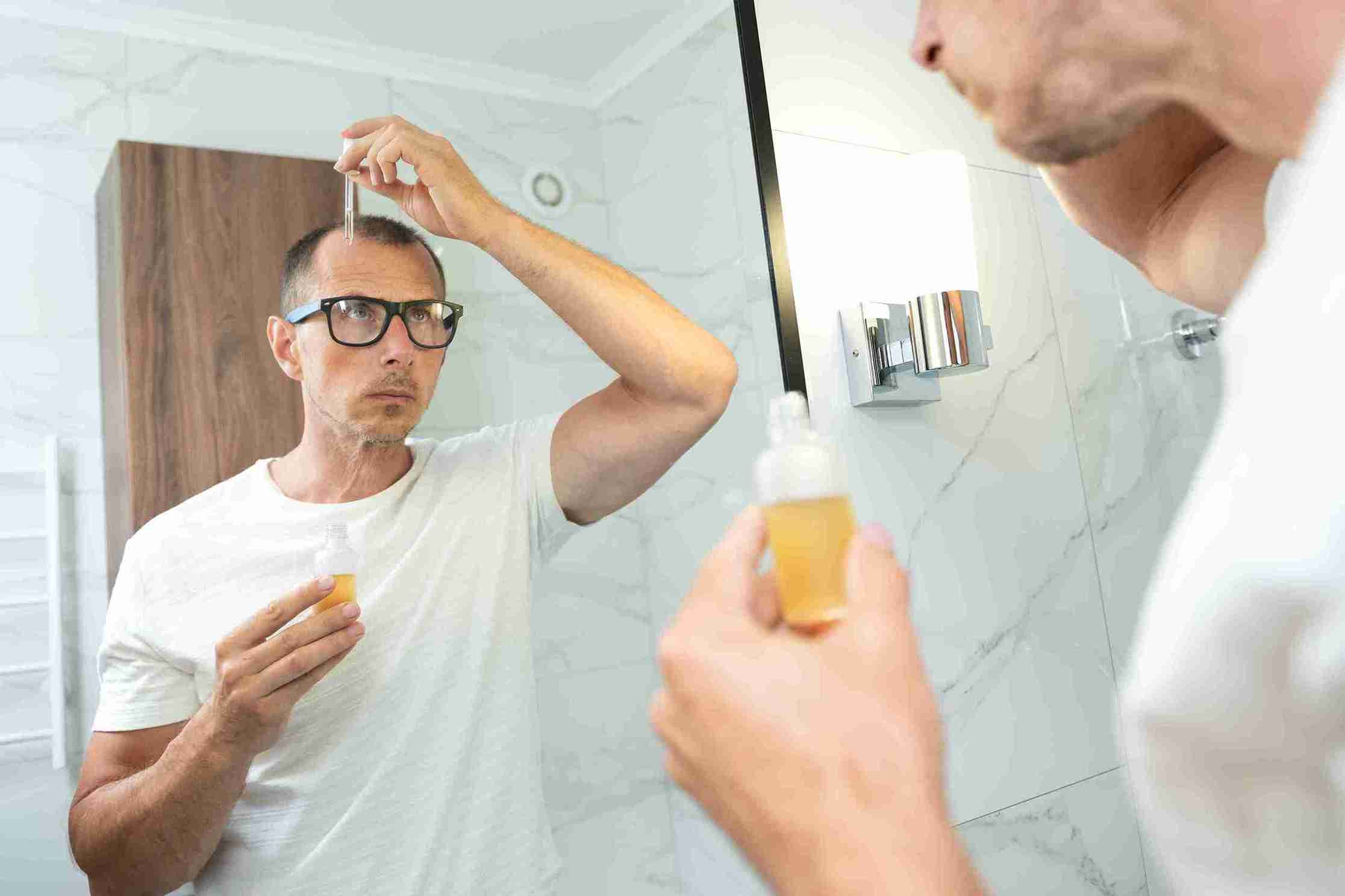 Hombre aplicando un suero en el cuero cabelludo frente al espejo en el baño.