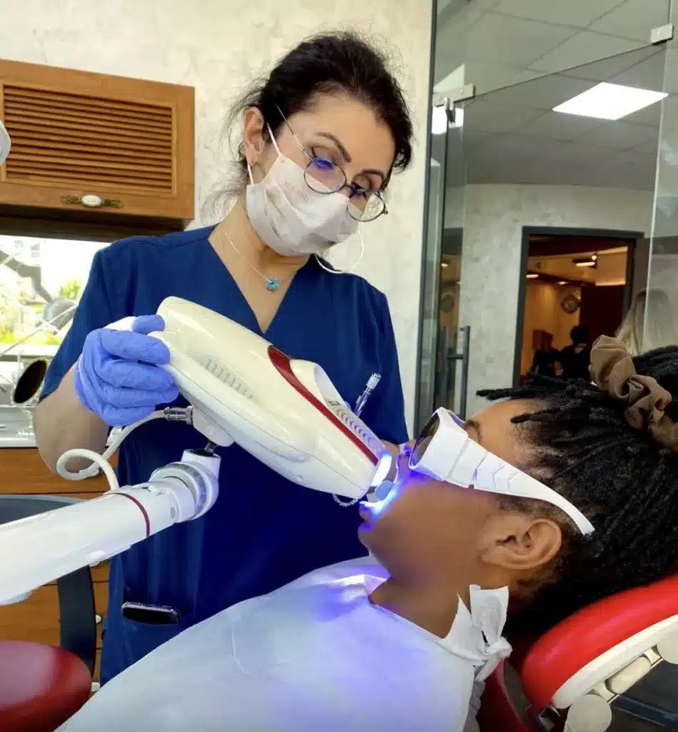 Zahnärztin führt eine professionelle Zahnaufhellung mit Bleaching-Lampe durch, Patient trägt Schutzbrille während der Behandlung.