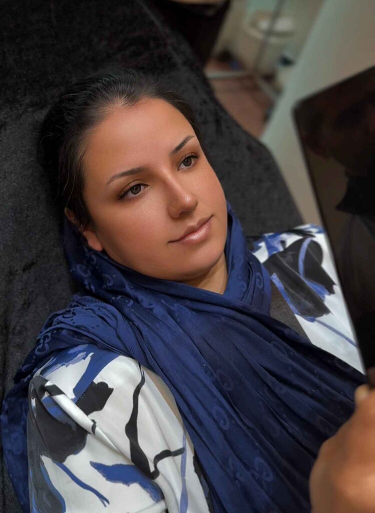 Woman calmly looking into a mirror after rhinoplasty.