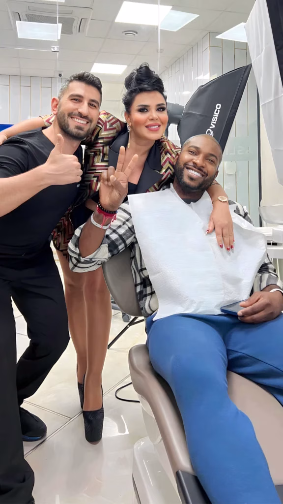 Paciente sonriente sentado en una clínica de trasplante capilar, acompañado por dos miembros del equipo médico que posan felices y muestran gestos positivos, reflejando una experiencia satisfactoria.