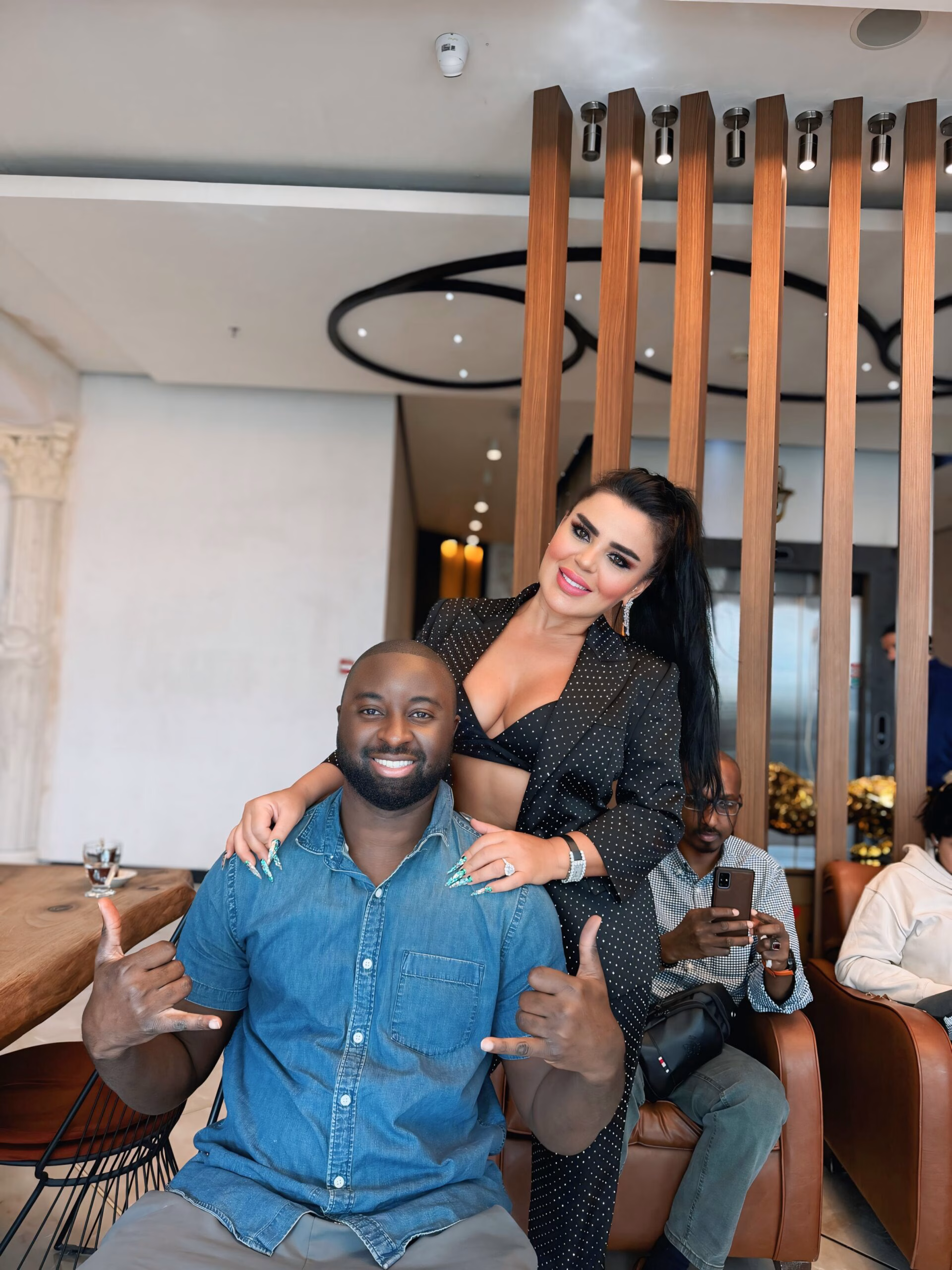 Hombre sonriente con cabello corto junto a una mujer elegante posando en una sala moderna, en un contexto relacionado con injerto capilar afro.