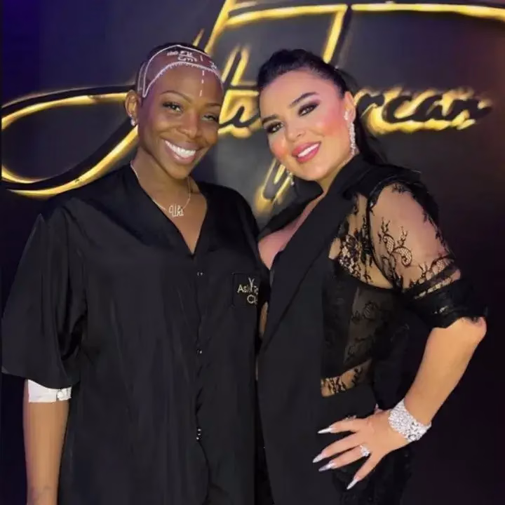 Dos mujeres sonriendo frente al logo de una clínica estética. Una de ellas lleva líneas de guía dibujadas en la cabeza, indicando preparación para un procedimiento capilar, mientras la otra aparece elegantemente vestida, posando junto a ella.